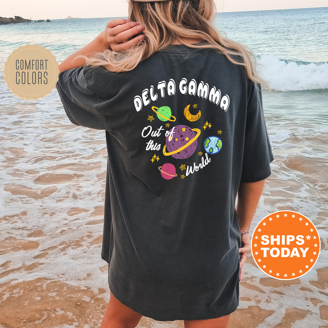 A woman wearing a black t-shirt with a colorful graphic design of planets and stars on the back, standing on a beach with the ocean in the background.