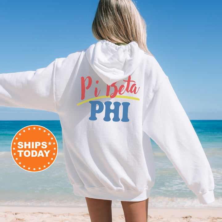 A woman wearing a white hoodie with the text "Pi beta phi" printed on it, standing on a beach with the ocean in the background.