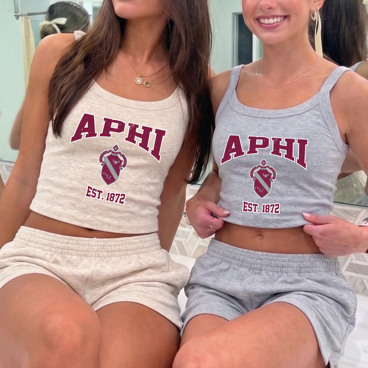 Two women wearing matching APHI tank tops and shorts are smiling and posing together.