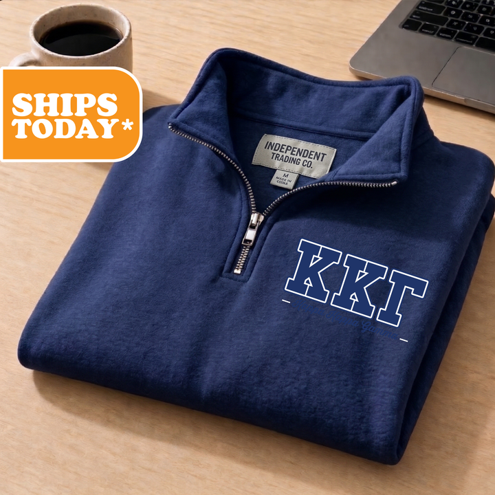 A navy blue sweatshirt with the letters "KKT" printed on it, placed on a wooden surface next to a laptop and a coffee cup.