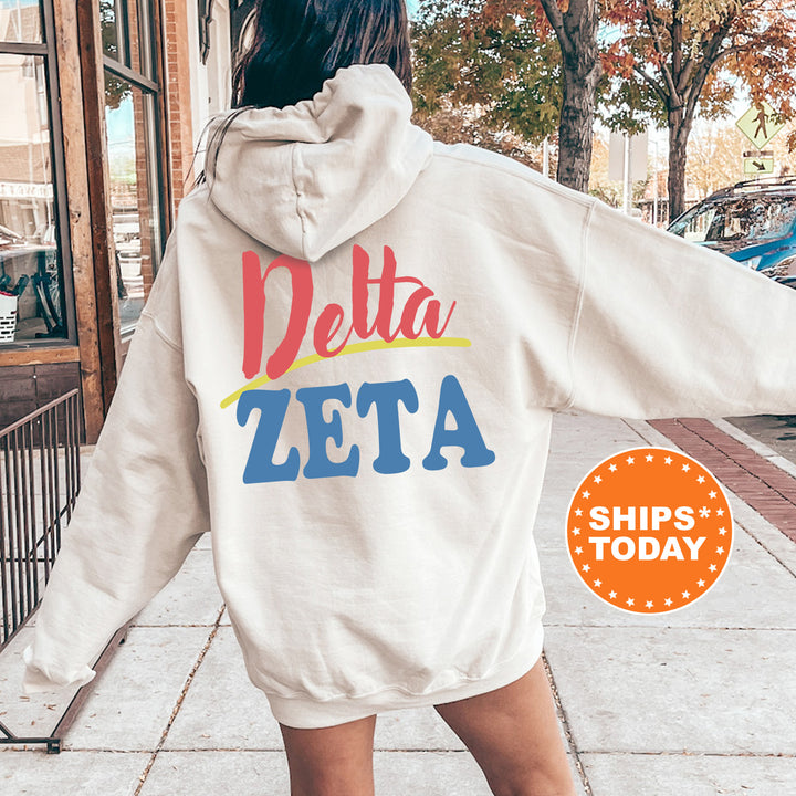 A person wearing a white hoodie with the Delta Zeta logo printed on it, standing on a sidewalk with a car and trees in the background.