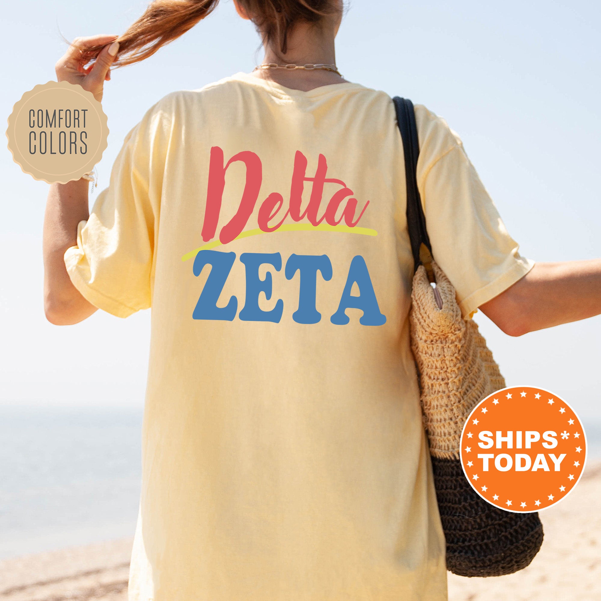 A woman wearing a yellow Delta Zeta t-shirt and carrying a woven bag stands on a beach, with a sign advertising 