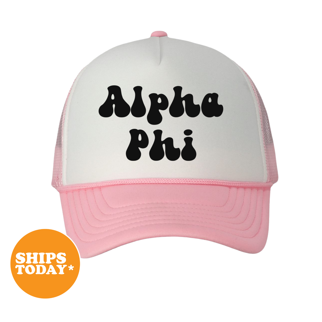 A white and pink baseball cap with the text "Alpha Phi" printed on it.