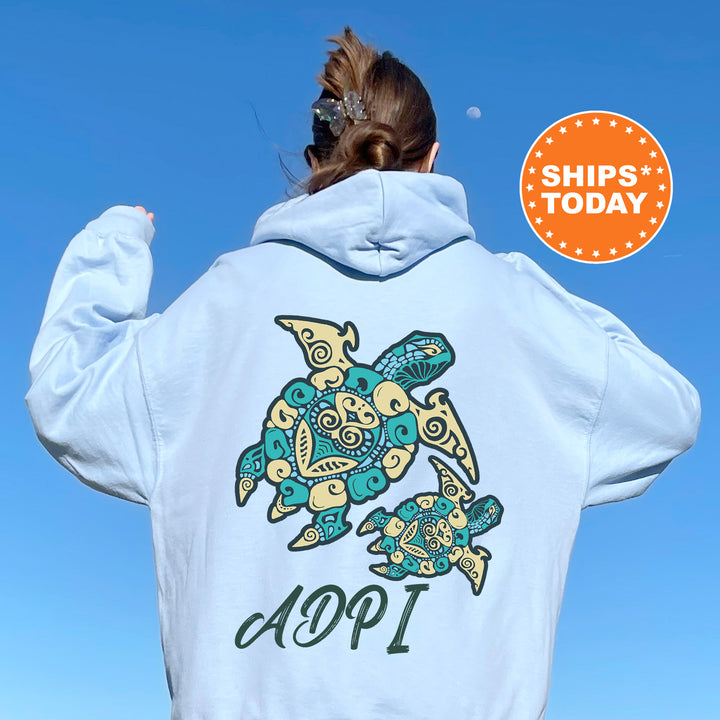 A person wearing a white hoodie with a colorful turtle design and the text "ADPI" printed on it, standing against a clear blue sky.