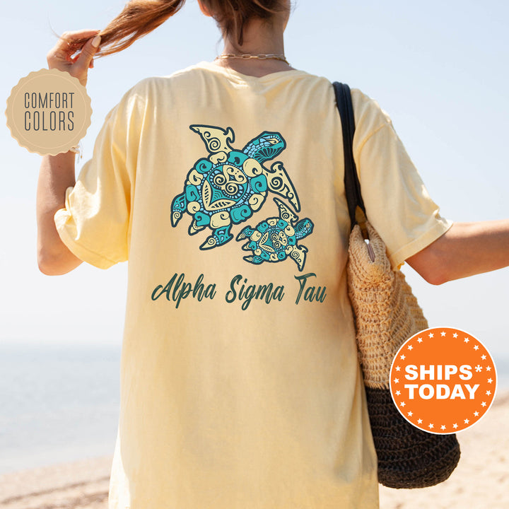 A person wearing a yellow t-shirt with a turtle design and text, standing on a beach with a handbag.