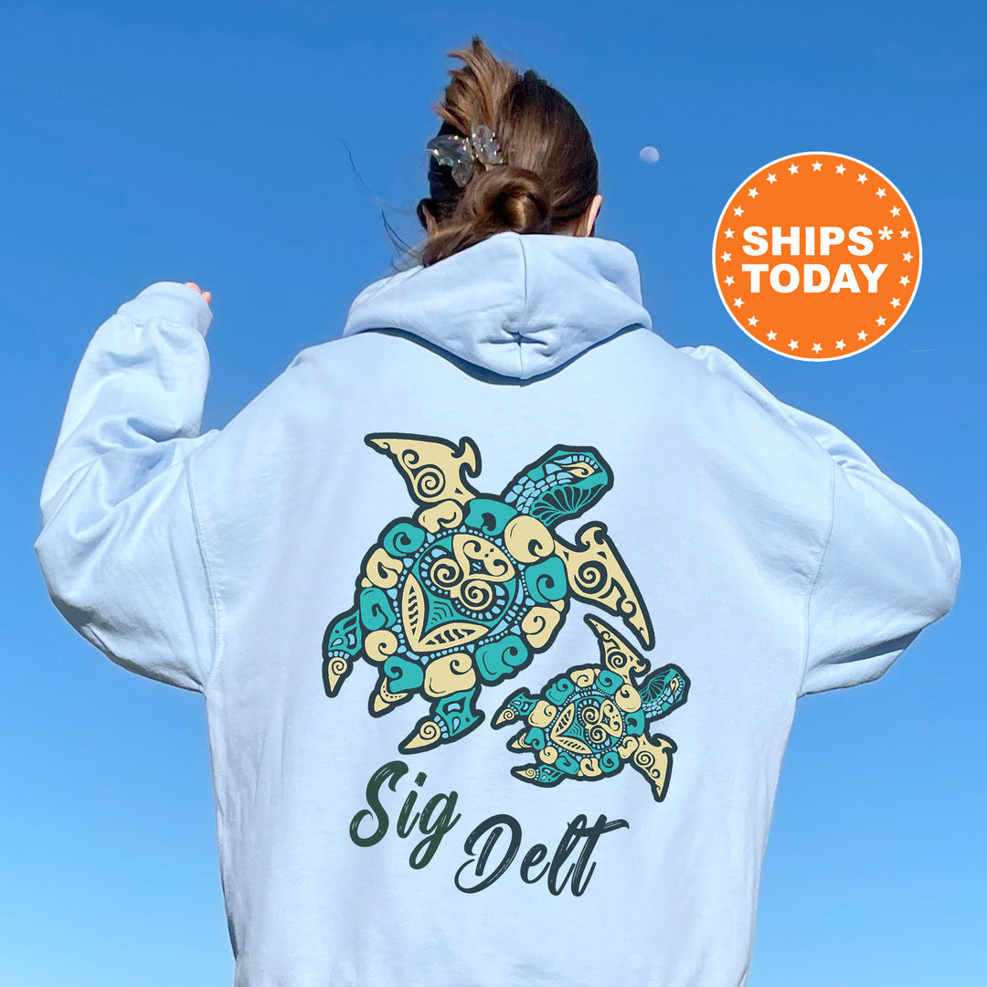 A person wearing a light blue hoodie with a graphic of a turtle and the text "Sign Delt" printed on it, standing against a clear blue sky.