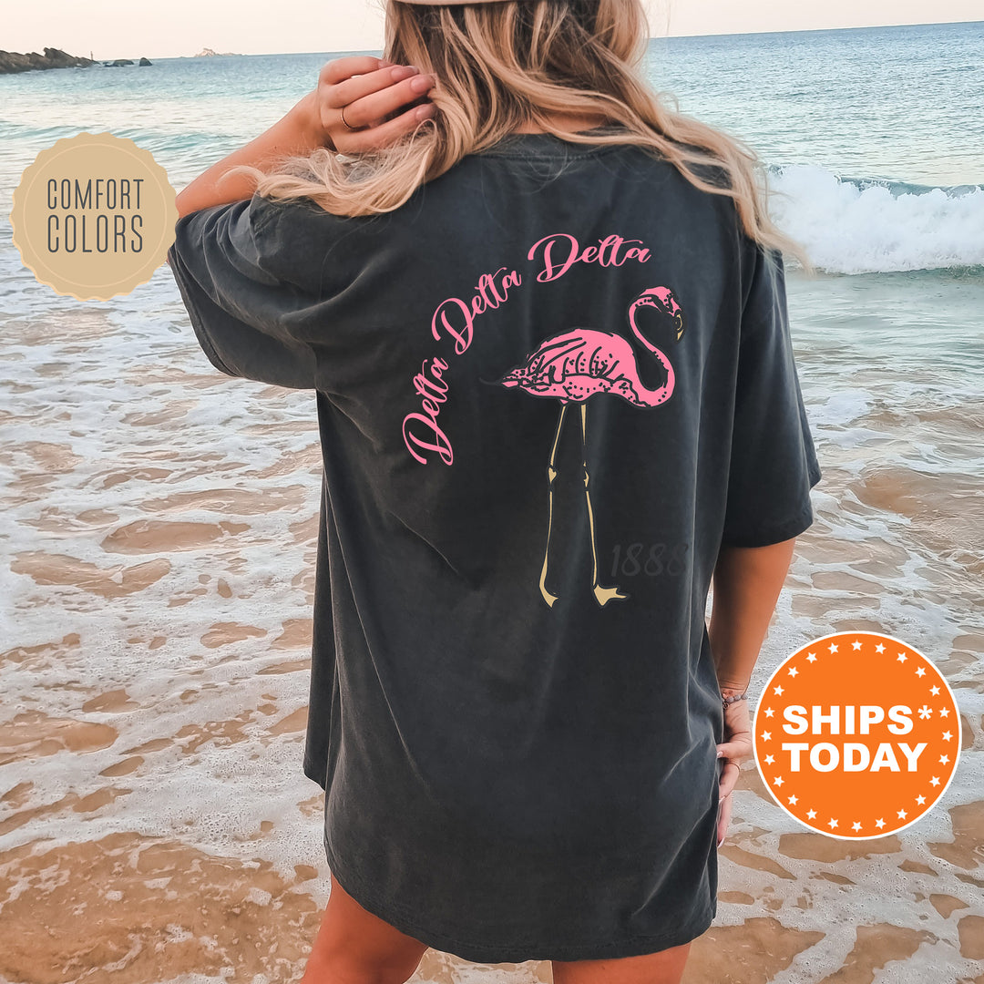a woman standing on a beach wearing a black shirt with a pink flamingo on