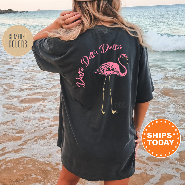 a woman standing on a beach wearing a black shirt with a pink flamingo on