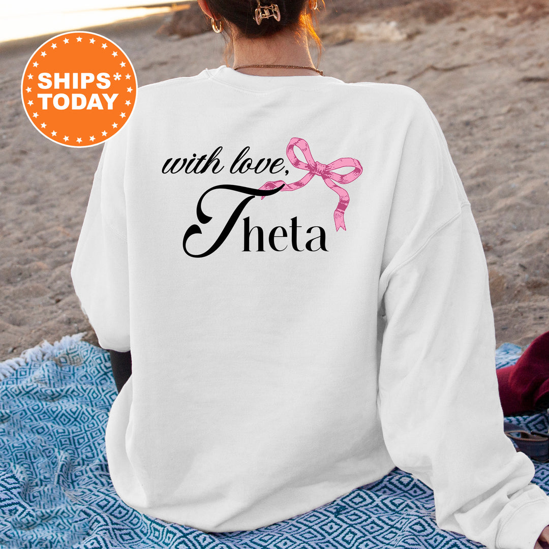 a woman sitting on the beach wearing a white sweatshirt with a pink ribbon