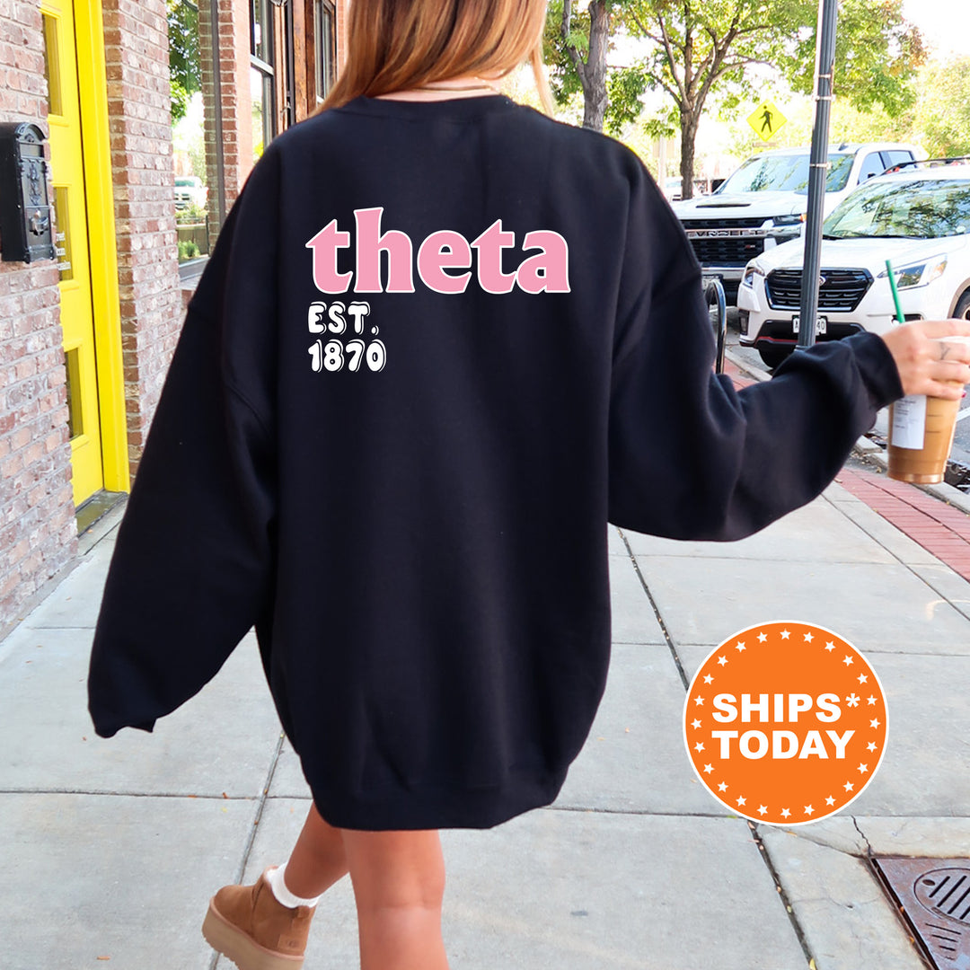 A person wearing a black sweatshirt with the text "theta EST 1870" printed on it, walking on a sidewalk.