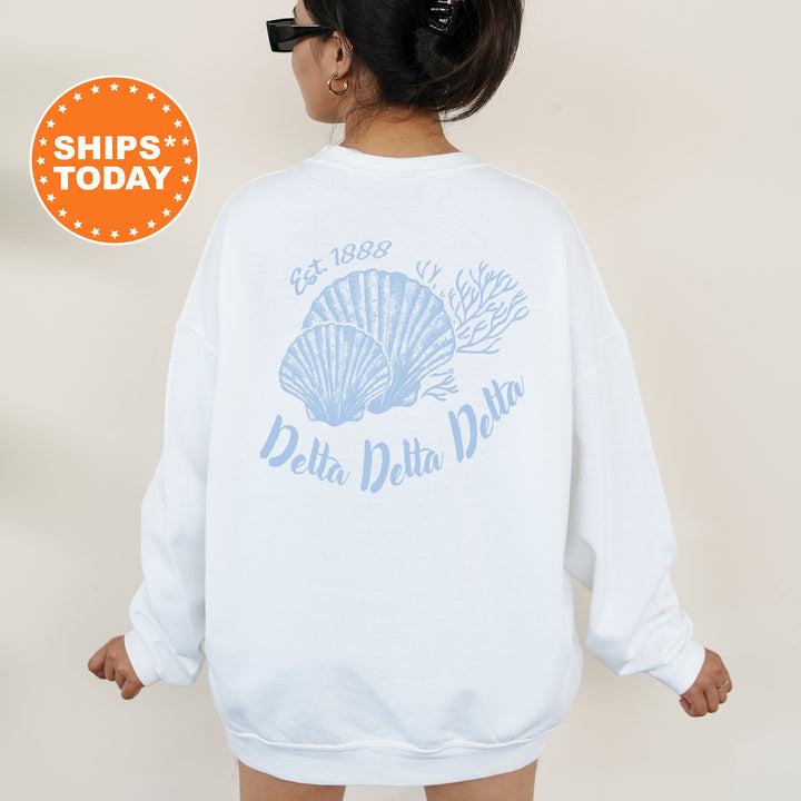A woman wearing a white sweatshirt with a blue design featuring a shell and the text "Delta Delta" printed on it.