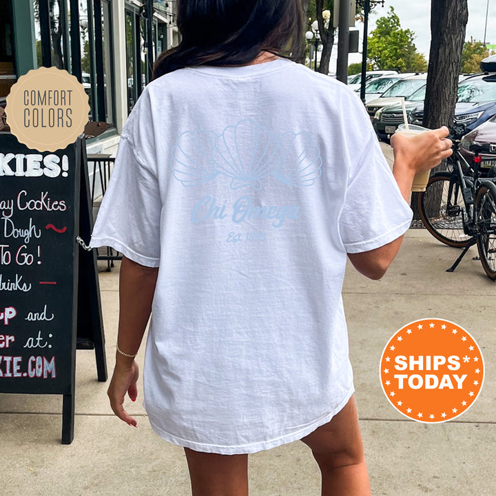 A person wearing a white t-shirt with a graphic design is walking on a sidewalk, with a chalkboard sign and bicycles visible in the background.