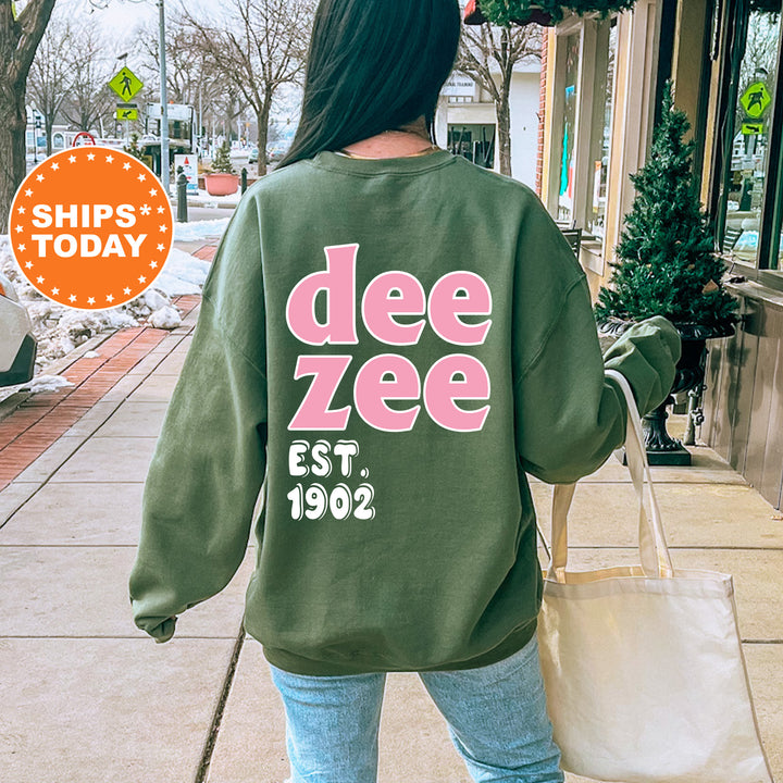 A person wearing a green sweatshirt with the text "dee zee EST. 1902" printed on it, walking on a sidewalk.