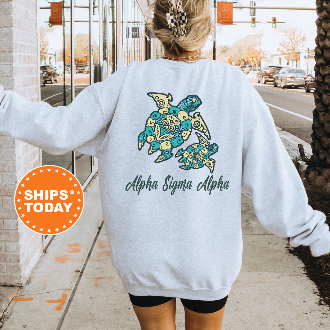 A person wearing a white sweatshirt with a graphic of a turtle and the text "Alpha Sigma Alpha" printed on it, standing on a sidewalk.