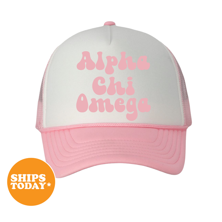 A pink and white baseball cap with the text "Alpha Chi Omega" printed on it.