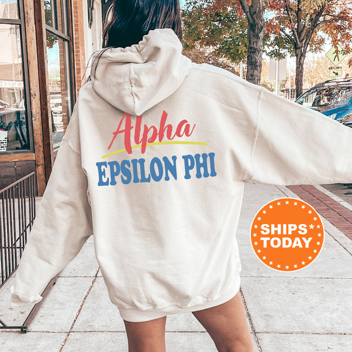 A person wearing a white hoodie with the text "Alpha Epson Phi" printed on it, standing on a sidewalk with a car and trees in the background.