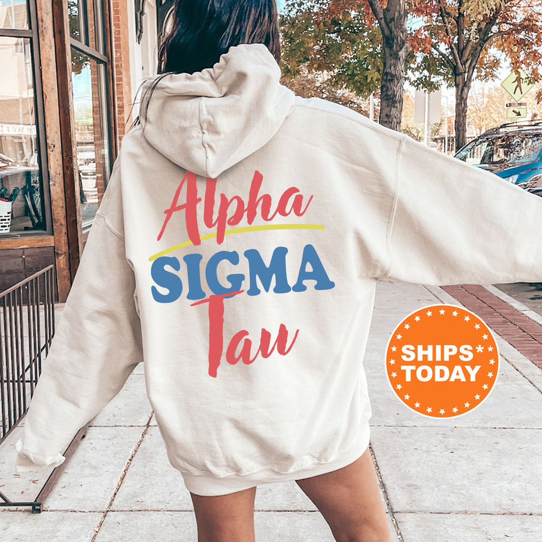 A person wearing a white hoodie with the text "Alpha Sigma Tau" printed on it, standing on a sidewalk with trees and a building in the background.