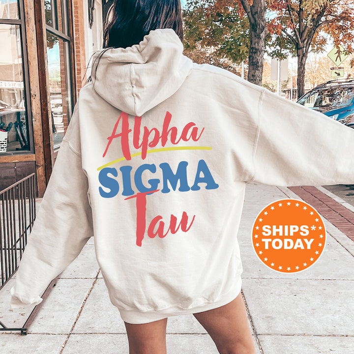 A person wearing a white hoodie with the text "Alpha Sigma Tau" printed on it, standing on a sidewalk with trees and a building in the background.