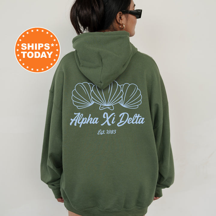 A person wearing a green hoodie with the text "Alpha Ki Delta" printed on it, along with a graphic of three shells.