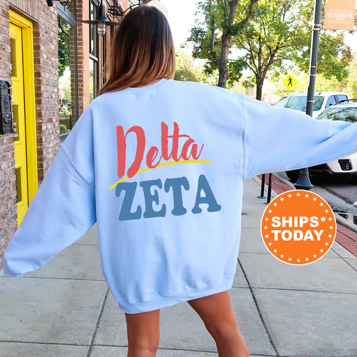 A woman wearing a blue sweatshirt with the text "Delta Zeta" printed on it, standing on a sidewalk.