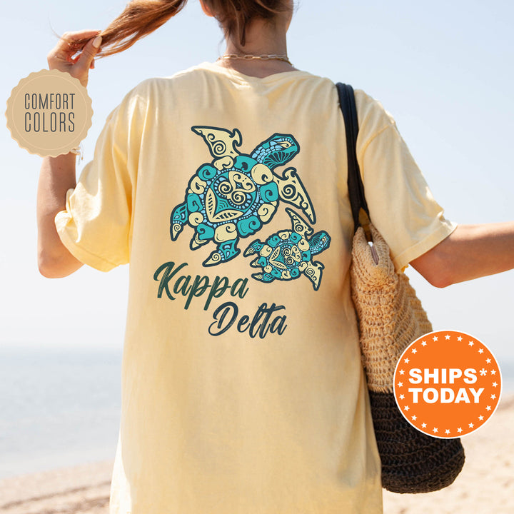 A person wearing a yellow t-shirt with a turtle design and text, standing on a beach with a handbag.