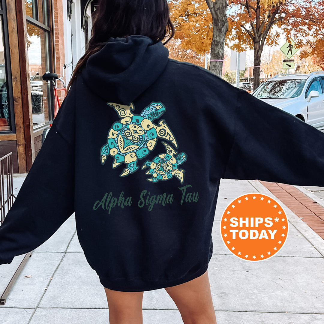 A person wearing a black hoodie with a graphic of a turtle and the text "Alpha Sigma Tau" printed on it, standing on a sidewalk.