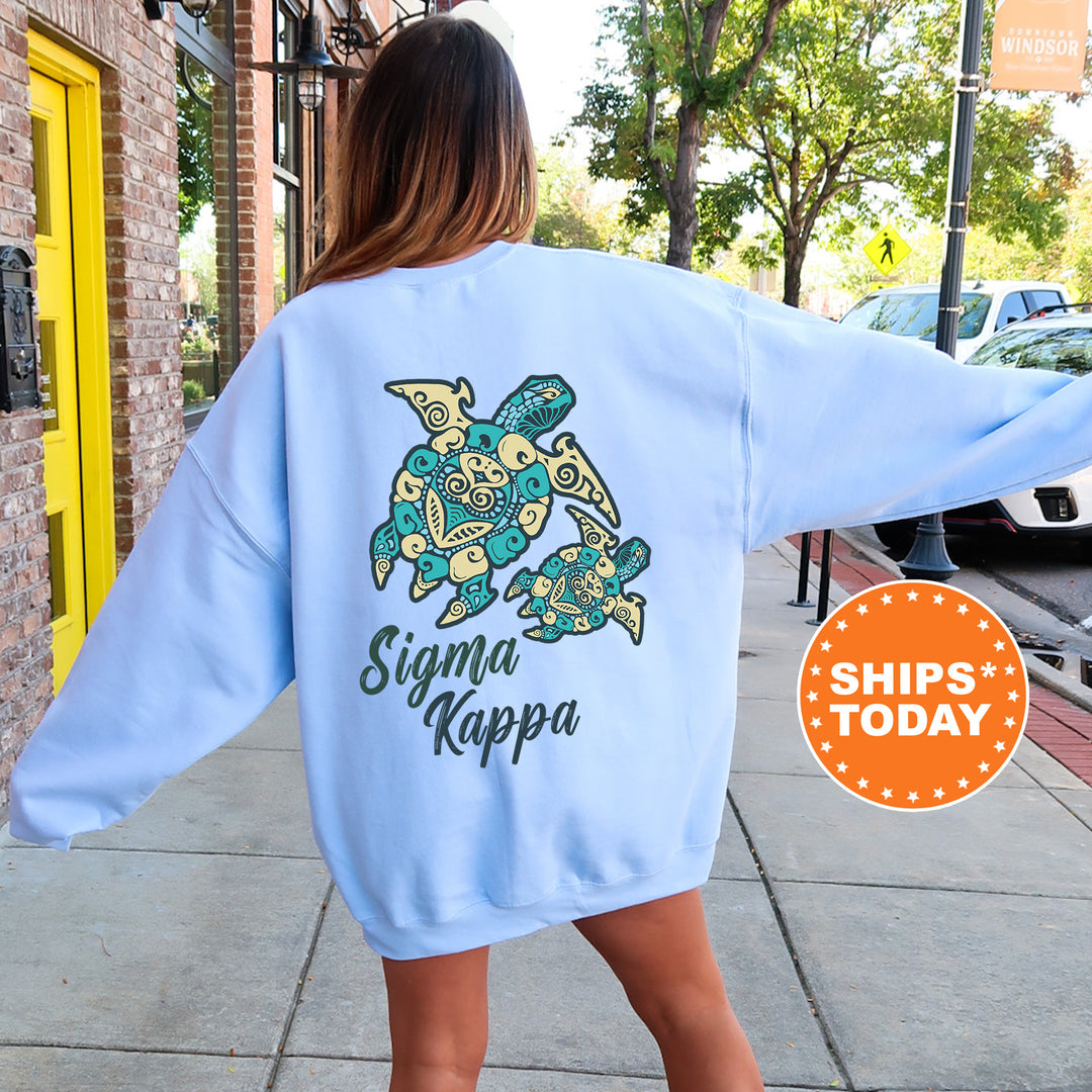 A woman wearing a light blue sweatshirt with a graphic of a turtle and the text " Sigma Kappa" printed on it, standing on a sidewalk.