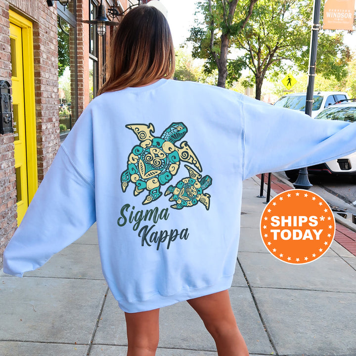 A woman wearing a light blue sweatshirt with a graphic of a turtle and the text " Sigma Kappa" printed on it, standing on a sidewalk.