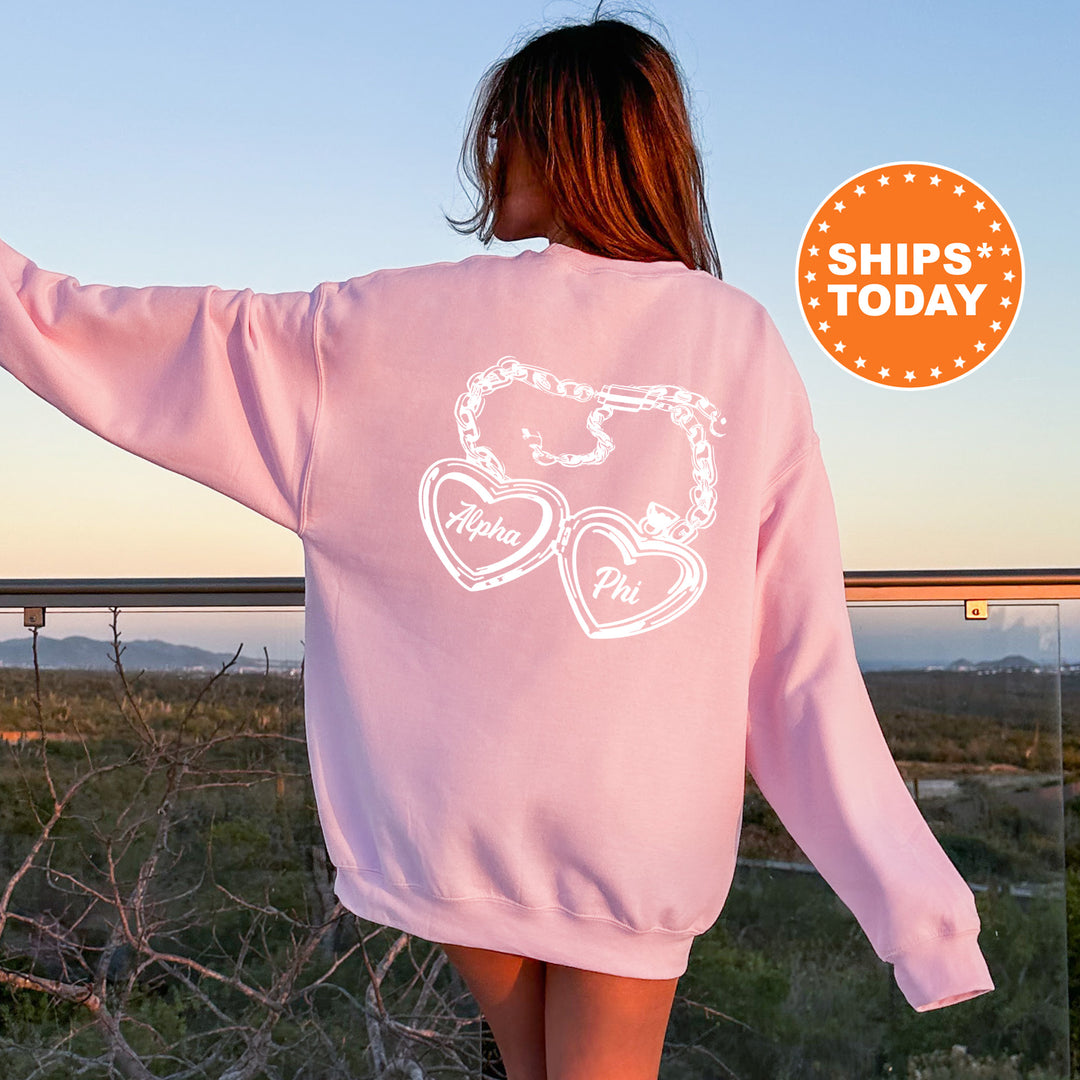 A woman wearing a pink sweatshirt with a graphic design on the back, standing in front of a scenic outdoor landscape.
