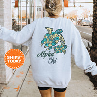 A person wearing a grey sweatshirt with a colorful turtle design and text on the back, standing on a sidewalk with a traffic light in the background.