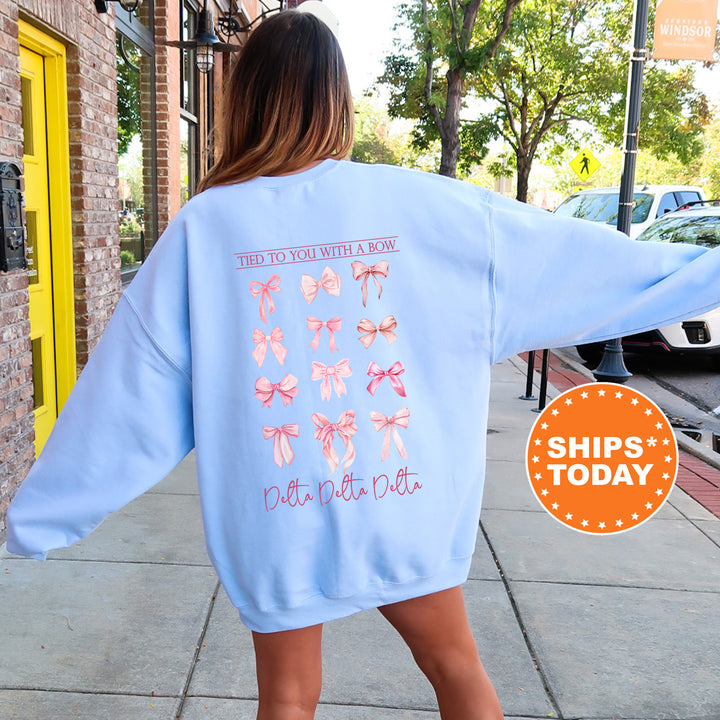 A woman wearing a light blue sweatshirt with a graphic design of pink bows on the back, standing on a sidewalk.