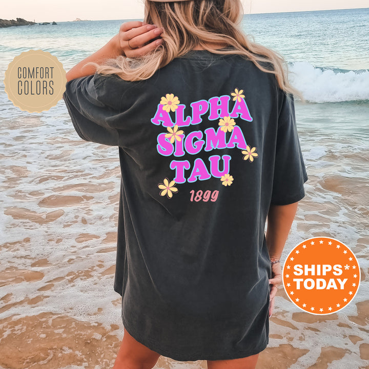 A woman wearing a black t-shirt with the text "ALPHA SIGMA TAU 1899" printed on it, standing on a beach with the ocean in the background.