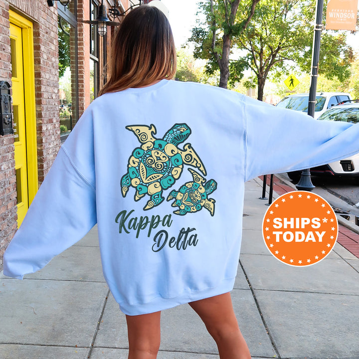 A woman wearing a light blue sweatshirt with a graphic of a turtle and the text "Kappa Delta" printed on it, standing on a sidewalk.
