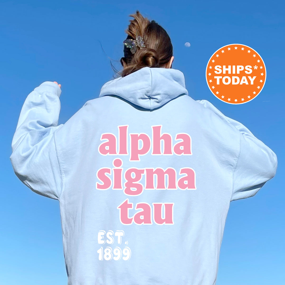 A person wearing a light blue hoodie with the text "Alpha Sigma Tau" printed on it, standing against a clear blue sky.