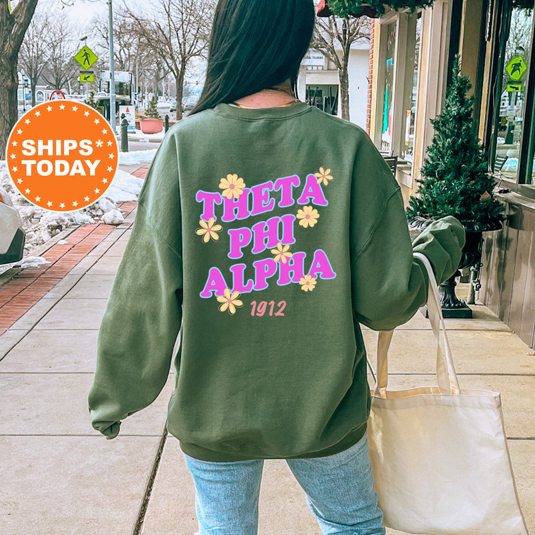 A woman wearing a green sweatshirt with the text "THETA PHI ALPHA 1912" printed on it, walking down a city street.