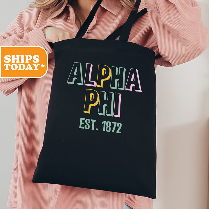 a woman holding a black tote bag with the words alpha phu est