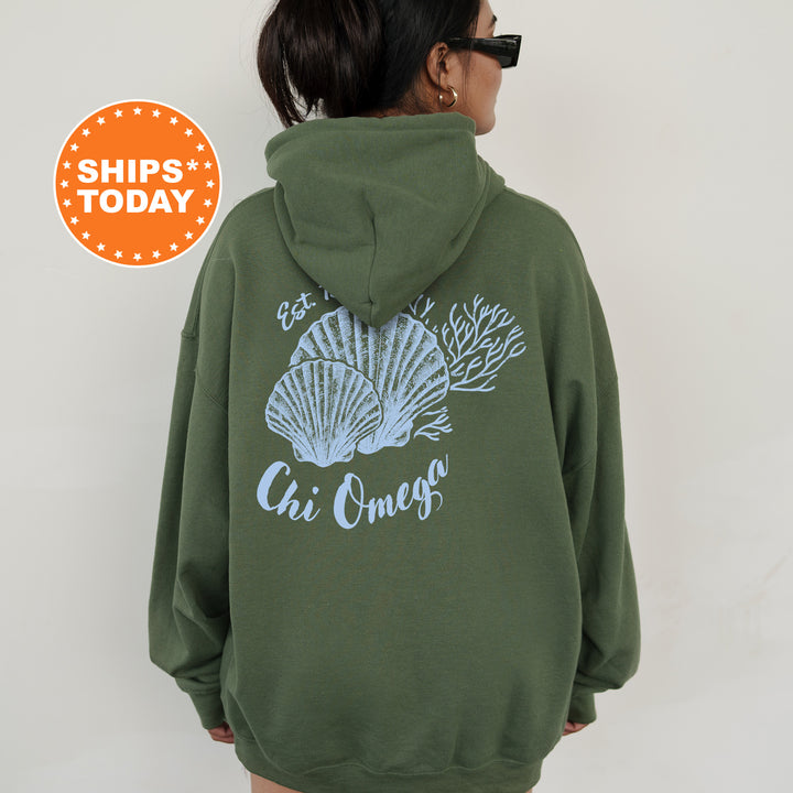 A person wearing a green hoodie with a graphic of seashells and the text "Chi Omega" printed on it.