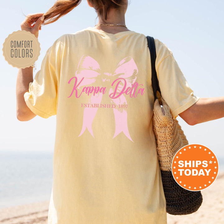 a woman is walking on the beach with a pink bow on her shirt