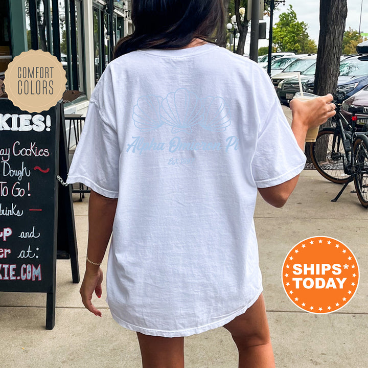A person wearing a white t-shirt with a graphic design on the back is walking on a sidewalk, with a chalkboard sign and bicycles visible in the background.