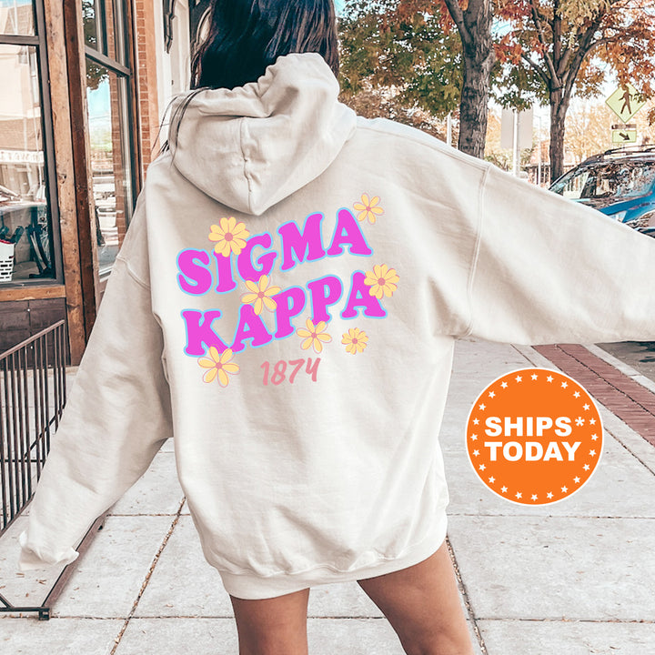 A person wearing a white hoodie with the text "SIGMA KAPPA 1874" printed on it, standing on a sidewalk with trees and a building in the background.