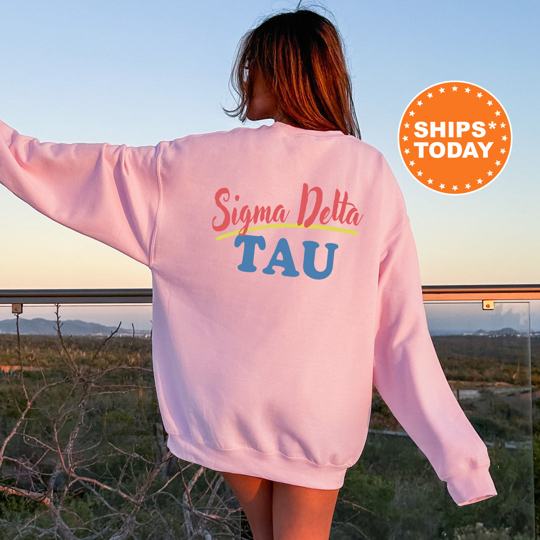 A woman wearing a pink sweatshirt with the text " Sigma Delta Tau" printed on it, standing on a balcony overlooking a scenic landscape.