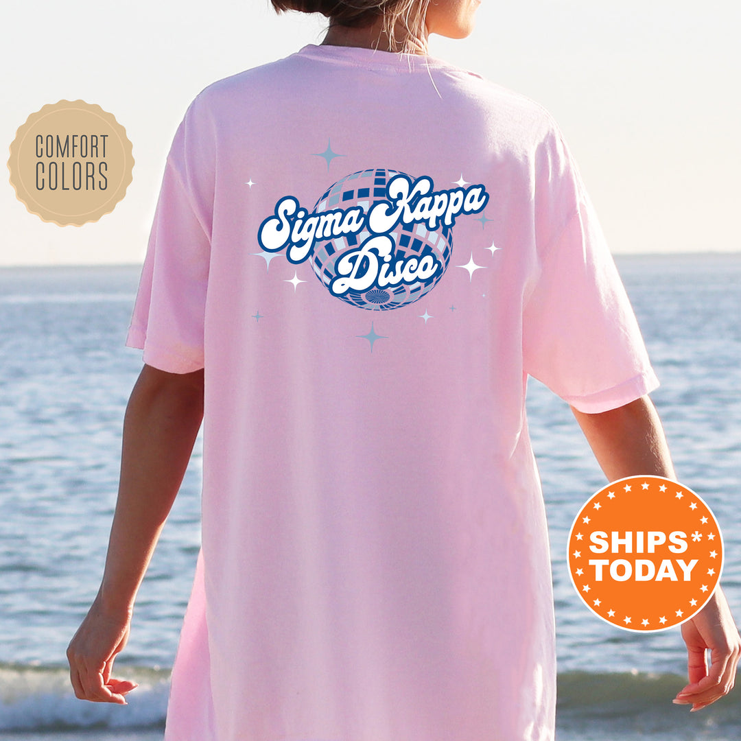 A person wearing a pink t-shirt with the text " Sigma Kappa D disco" printed on it, standing near the ocean.