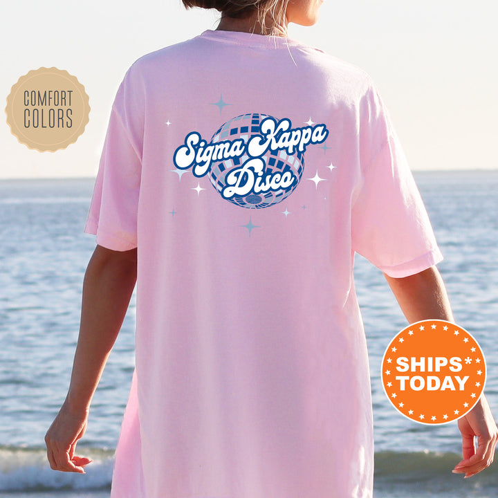 A person wearing a pink t-shirt with the text " Sigma Kappa D disco" printed on it, standing near the ocean.