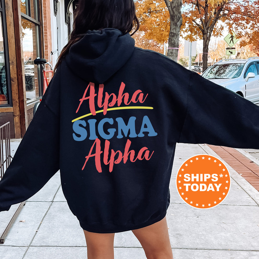 A person wearing a black hoodie with the text "Alpha Sigma Alpha" printed on it, standing on a sidewalk with a car and a building in the background.