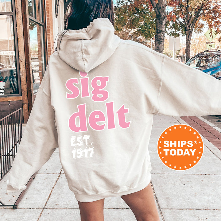 A person wearing a white hoodie with pink text and logos, standing on a sidewalk.