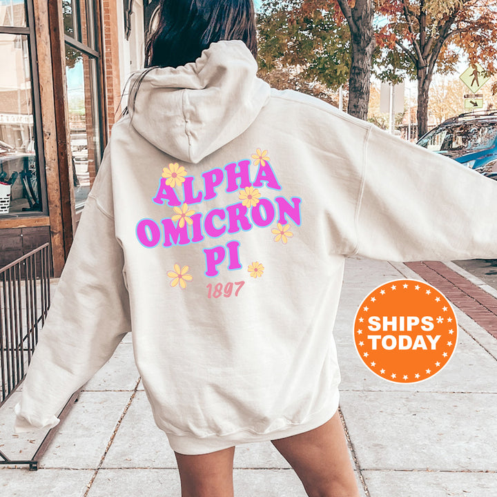 A person wearing a white hoodie with the text "ALPHA OMICRON PI" printed on it, standing on a sidewalk.