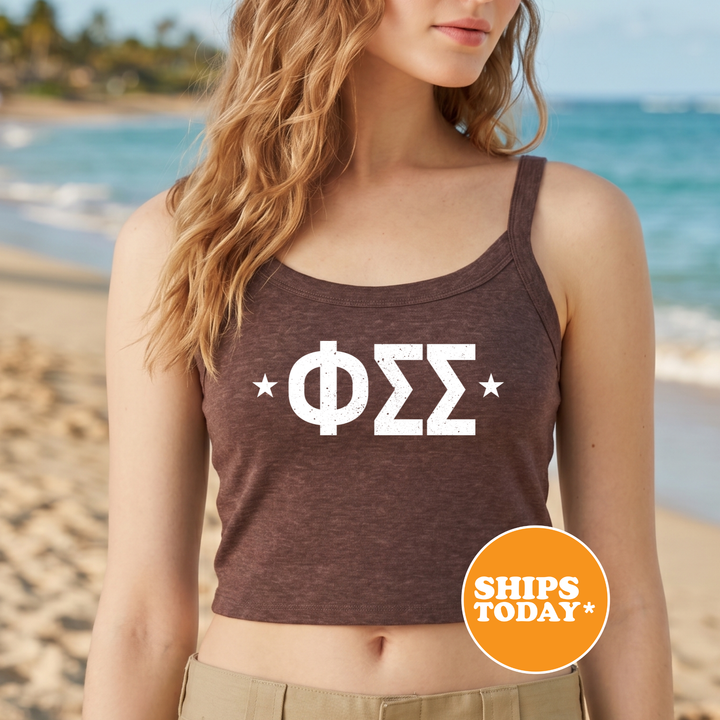 A woman wearing a brown tank top with the Greek letter Sigma (Σ) printed on it, standing on a beach with the ocean in the background.