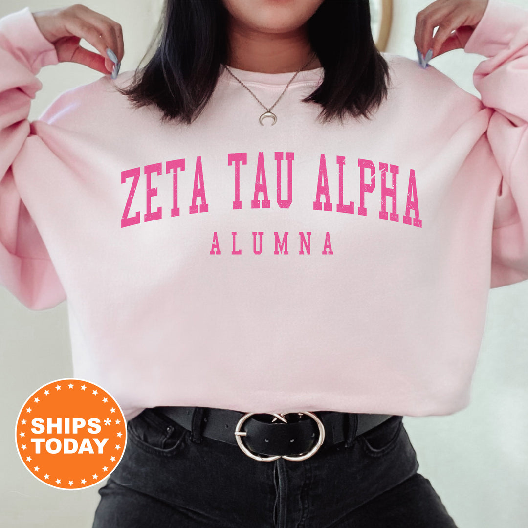 a woman wearing a pink sweatshirt with the word zeta tau alpha on it