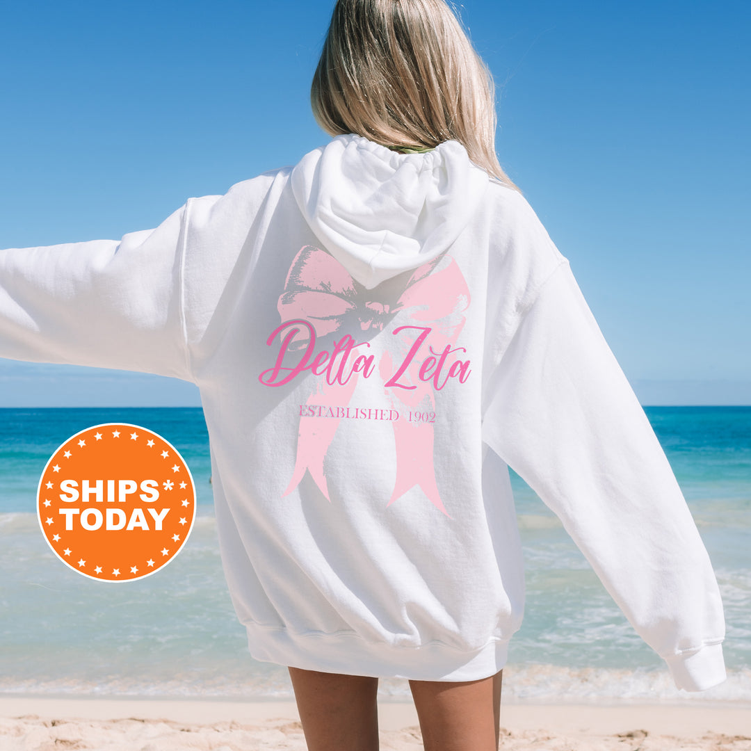 a woman standing on a beach wearing a white sweatshirt with a pink ribbon