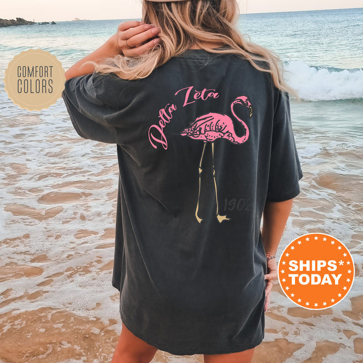 a woman standing on a beach wearing a black shirt with a pink flamingo on